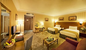 Ein Hotelzimmer mit einem Bett, einem Schreibtisch, einem Sessel, einem Fernseher und einer Obstschale.