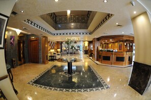 A hotel lobby with a central fountain, a reception desk, and a staircase.