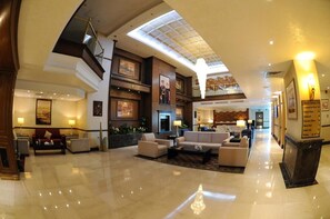 A spacious lobby with a high ceiling, a central seating area, and a staircase leading to an upper level.