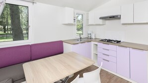 A compact kitchen with a dining area, a window with a view of trees, and a built-in stove.