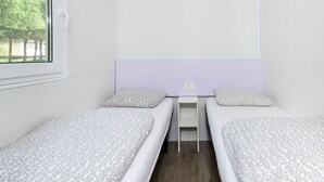 A small, single-room accommodation with two beds, a window, and a view of trees.