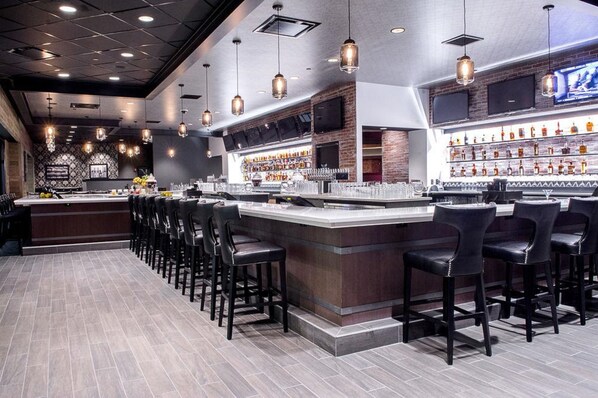 A bar area with a long counter, multiple bar stools, and a well-stocked shelf with bottles. - Caesars Southern Indiana Hotel Casino (Elizabeth)