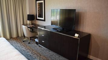A hotel room with a bed, a desk with a TV, a chair, and a framed picture on the wall.