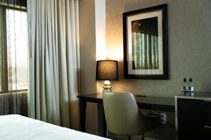 A hotel room with a bed, a desk with a lamp, a chair, a framed picture on the wall, and a window with curtains. - Caesars Southern Indiana Hotel Casino (Elizabeth)