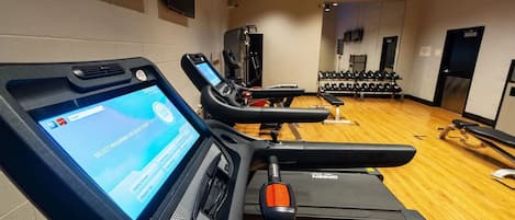 A gym with treadmills, weights, and a digital interface on one of the machines.