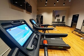 A gym with treadmills, weights, and a digital interface on one of the machines.