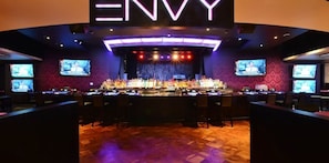 Zona de bar con varias pantallas, un escenario y una barra.