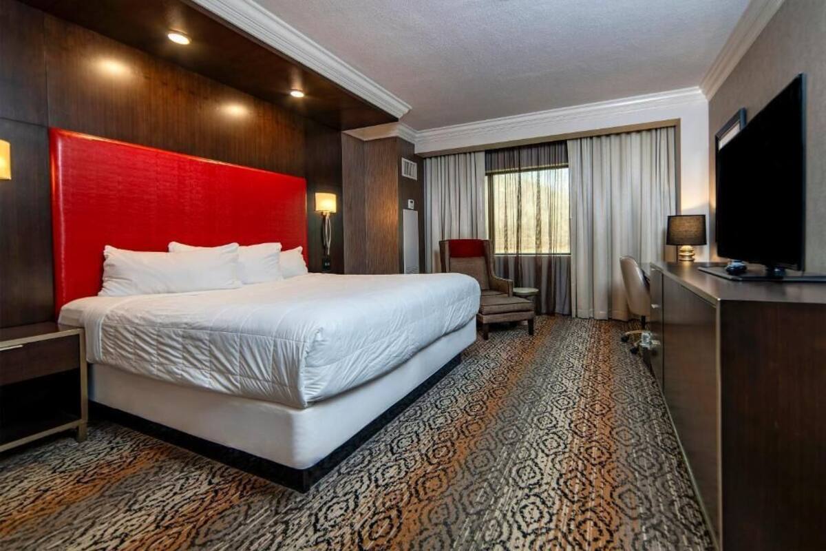 A hotel room with a large bed, a desk, a chair, a TV, and a window with curtains.