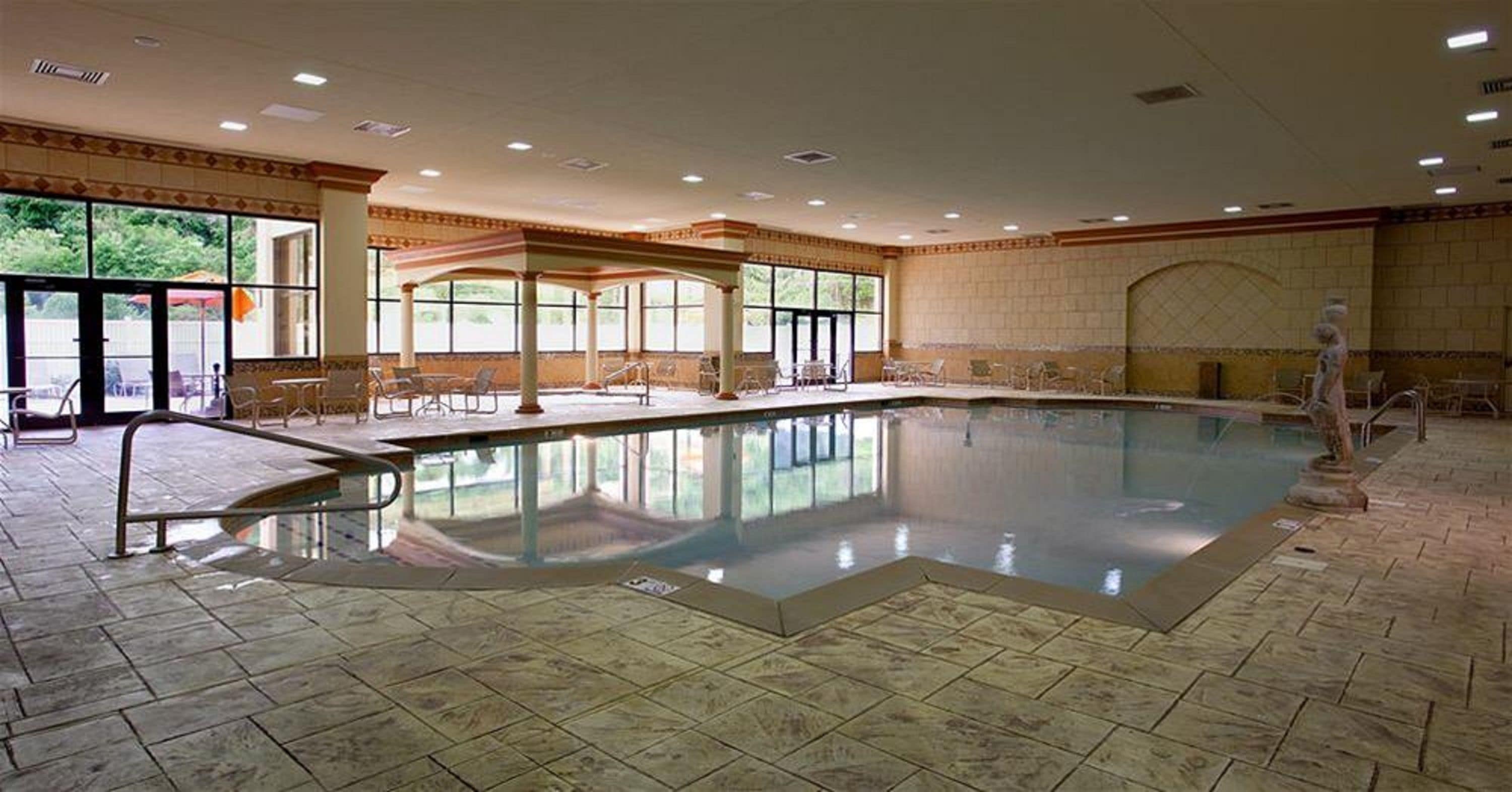 An indoor swimming pool with a tiled floor, large windows, and a covered seating area.