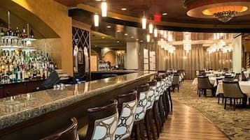 A bar area with a long counter and multiple chairs, a dining area with tables and chairs, and a chandelier.