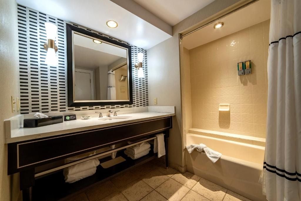 A bathroom with a double sink vanity, a large mirror, a bathtub, and a shower area.