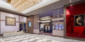 A hotel lobby with a modern design, featuring a patterned floor, a large chandelier, and a red accent wall with a gold emblem. - Caesars Southern Indiana Hotel Casino (Elizabeth)