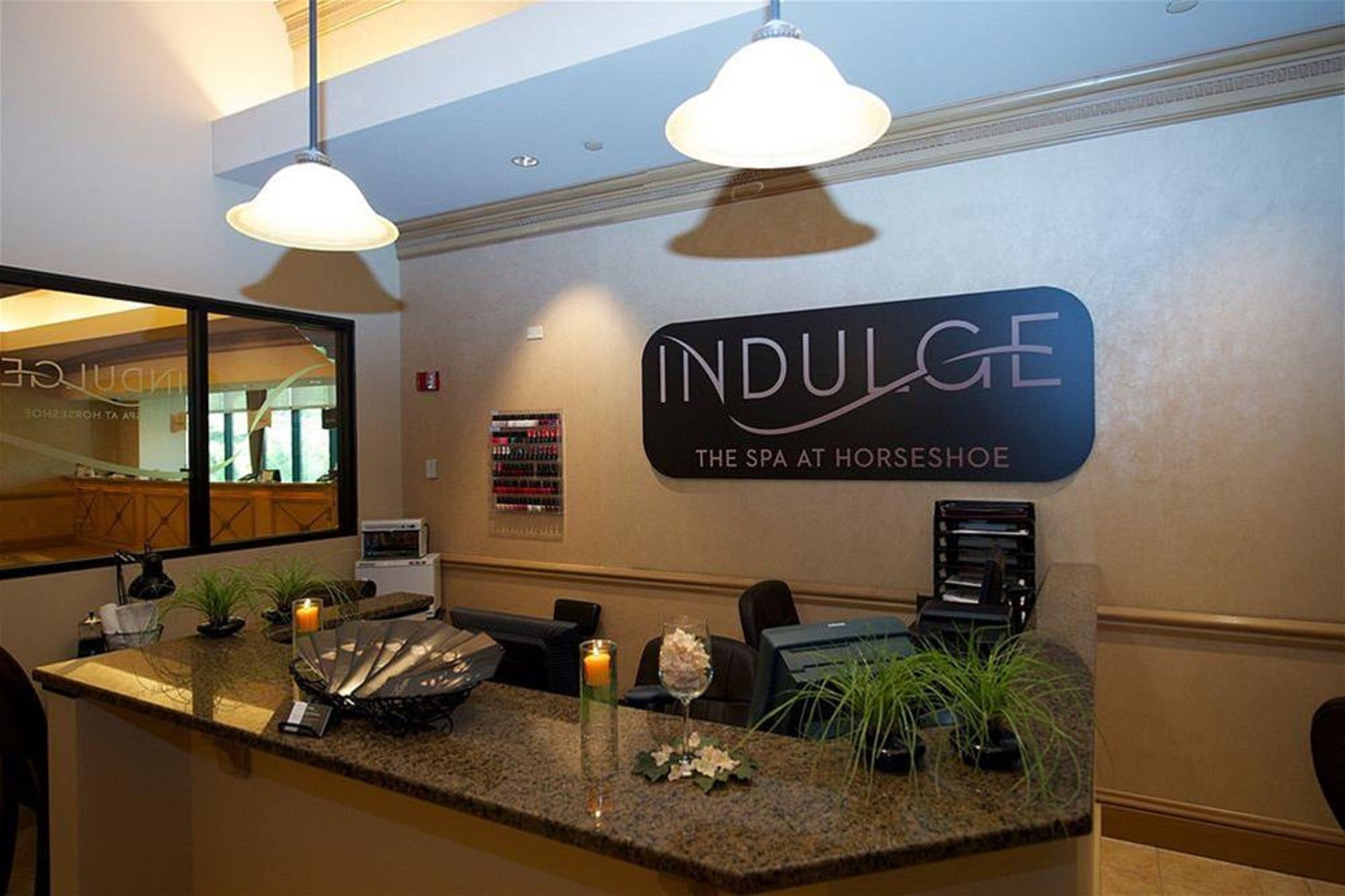 A reception area with a sign reading 'INDULGE THE SPA AT HORSESHOE,' a counter with a computer, a phone, and decorative items.
