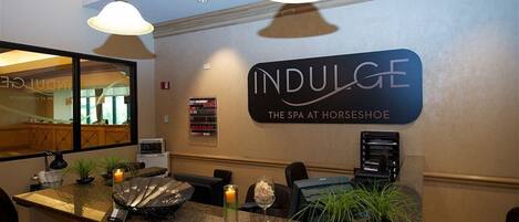 Een receptie met een bord waarop staat 'INDULGE THE SPA AT HORSESHOE', een balie met een computer, een telefoon en decoratieve objecten.
