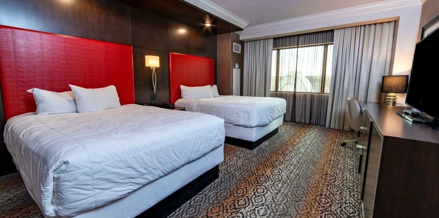 Habitació d'hotel amb dos llits, una taula de treball, televisió i finestra amb cortines.