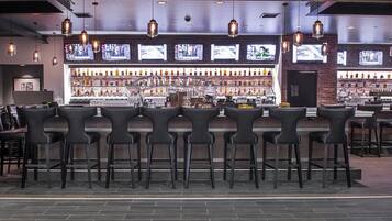 A bar area with multiple seating options, a well-stocked liquor shelf, and several televisions displaying content.