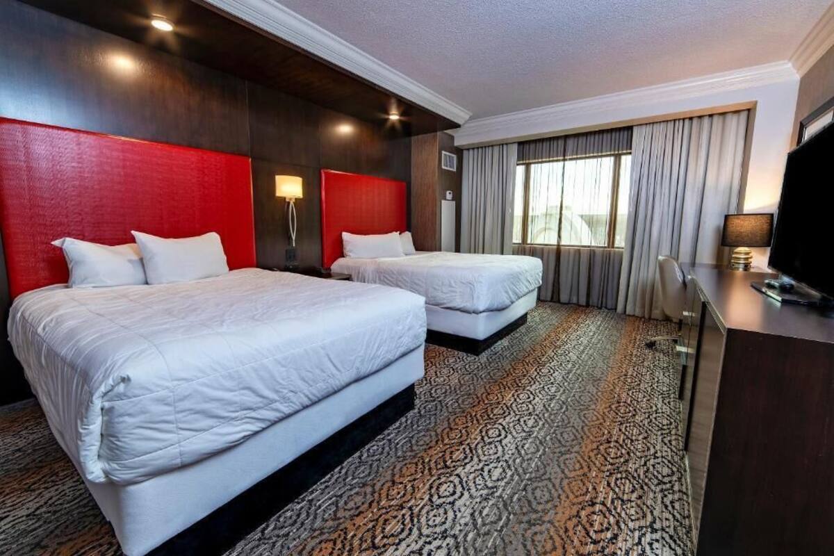 A hotel room with two beds, a desk, a TV, and a large window with curtains.