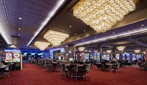 A casino with multiple gaming tables and slot machines, a non-smoking sign, and a red carpeted floor.
