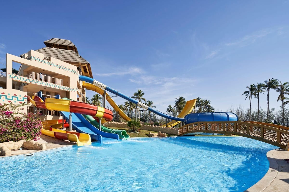 A water park with a large pool, multiple water slides, and a building with balconies.