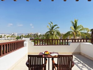 A balcony with a table, chairs, and a view of palm trees and buildings. - Juweira Boutique Hotel (Salalah)