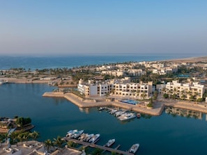 A coastal marina with boats docked, a large building with multiple balconies, and a clear view of the sea. - Juweira Boutique Hotel (Salalah)