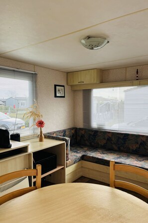 Ein kompaktes Wohnmobil-Interieur mit Esstisch, einer Bank, einem kleinen Schrank und einem Fenster mit Jalousien.