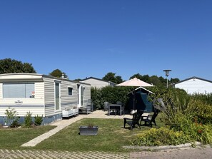 Ein Caravanpark mit Rasenfläche, Gartenmöbeln und einem kleinen Schuppen.
