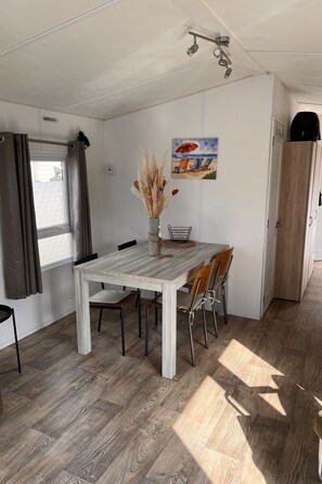 Ein Essbereich mit Tisch, Stühlen, einer Vase mit getrockneten Pflanzen, einem Gemälde an der Wand und einem Deckenventilator.