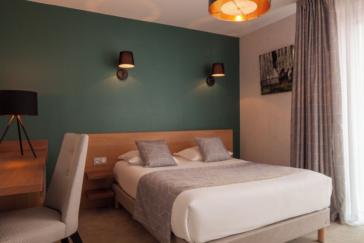 Une chambre d’hôtel équipée d’un lit, d’un bureau, d’une chaise et de deux lampes fixées au mur.