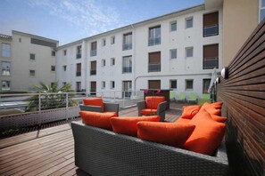 A rooftop terrace with wicker furniture and orange cushions, overlooking a building with multiple windows. - The Originals City, Les Thermes de L'avenue, Dax (Dax)