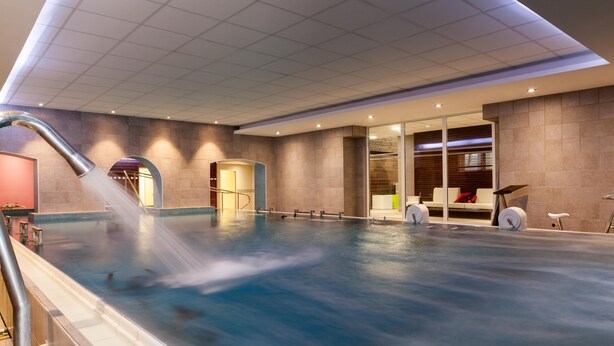 Una piscina interior con tobogán de agua, zona de sauna y sillón de masajes.