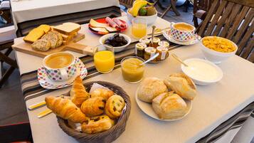 Una mesa de desayuno con pan, pasteles, fruta y bebidas.
