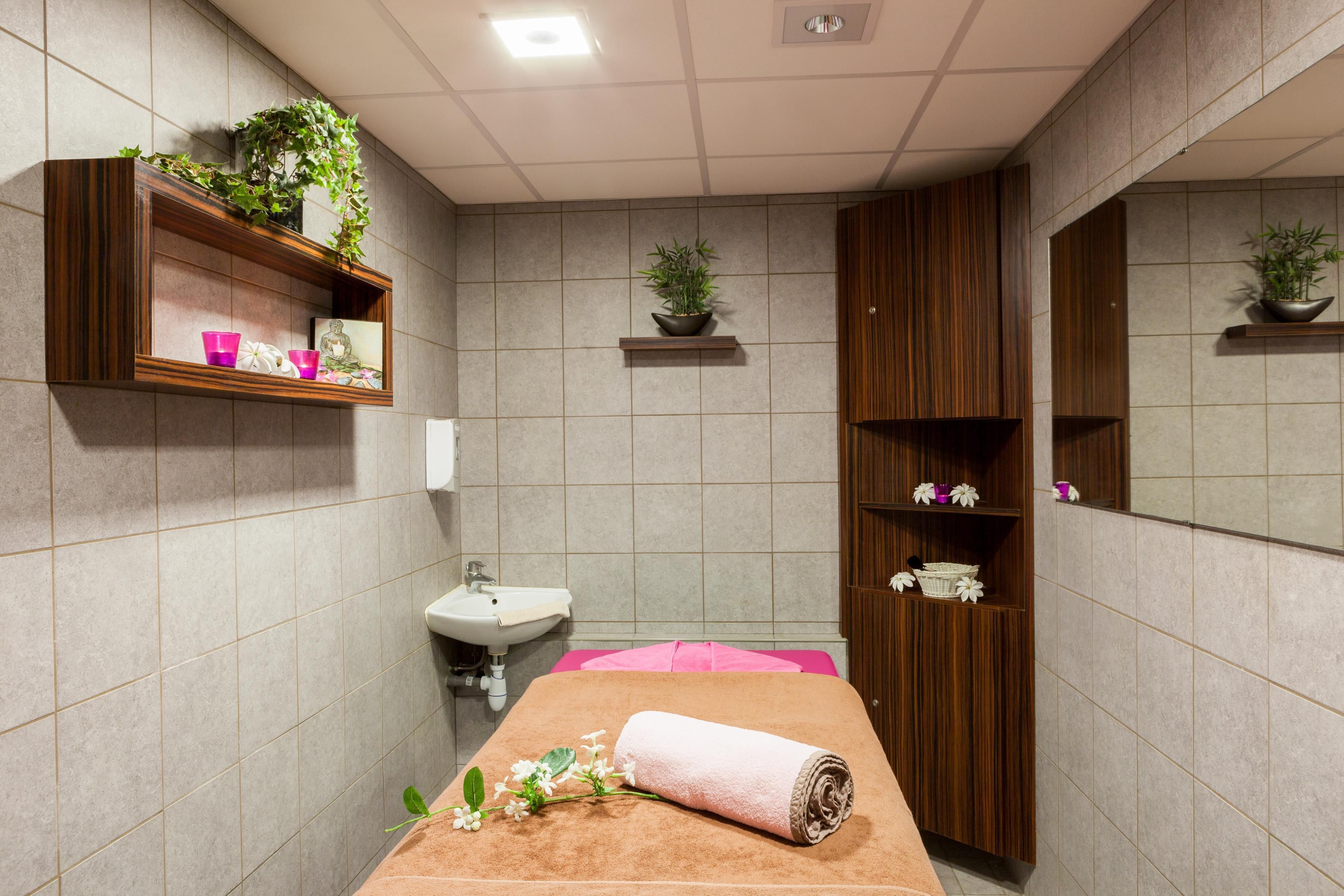 Ein Raum mit einer Massageliege, Pflanzenregalen, einem Waschbecken und Holzausbau.