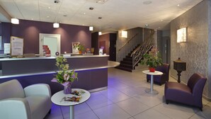 Zona de recepción con mostrador, sillas, una pequeña mesa con revistas y una escalera.