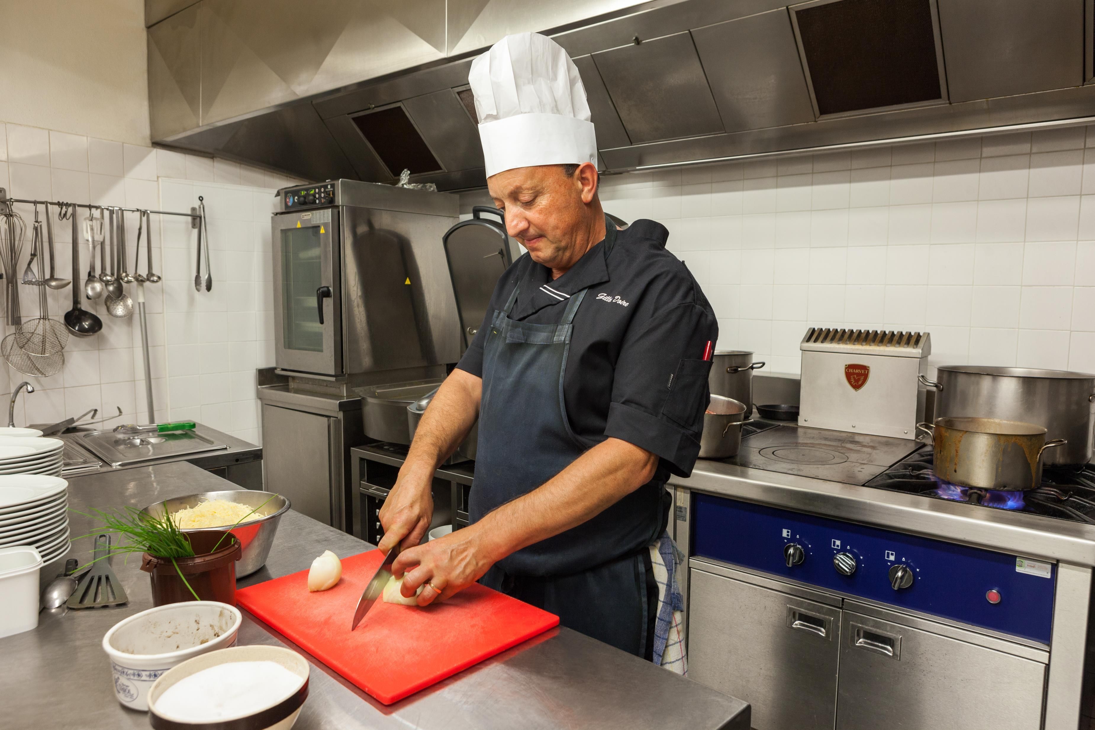 Un chef en una cocina profesional con electrodomésticos de acero inoxidable, una tabla de cortar roja y diversos utensilios de cocina.