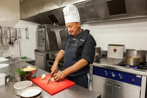 A chef in a professional kitchen with stainless steel appliances, a red cutting board, and various kitchen utensils. - The Originals City, Les Thermes de L'avenue, Dax (Dax)