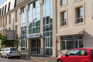Um edifício com grandes janelas, uma placa com 'Thermes de l'Avenue' e vários sinais de estacionamento.