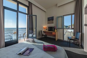 Ein Hotelzimmer mit Bett, Schreibtisch, Stuhl und einem Balkon mit Meerblick.