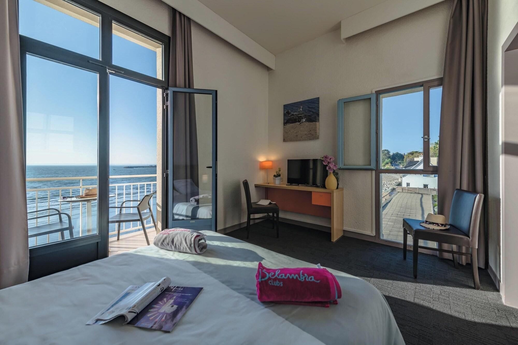 Une chambre d’hôtel équipée d’un lit, d’un bureau, d’une chaise et d’un balcon avec vue sur la mer.