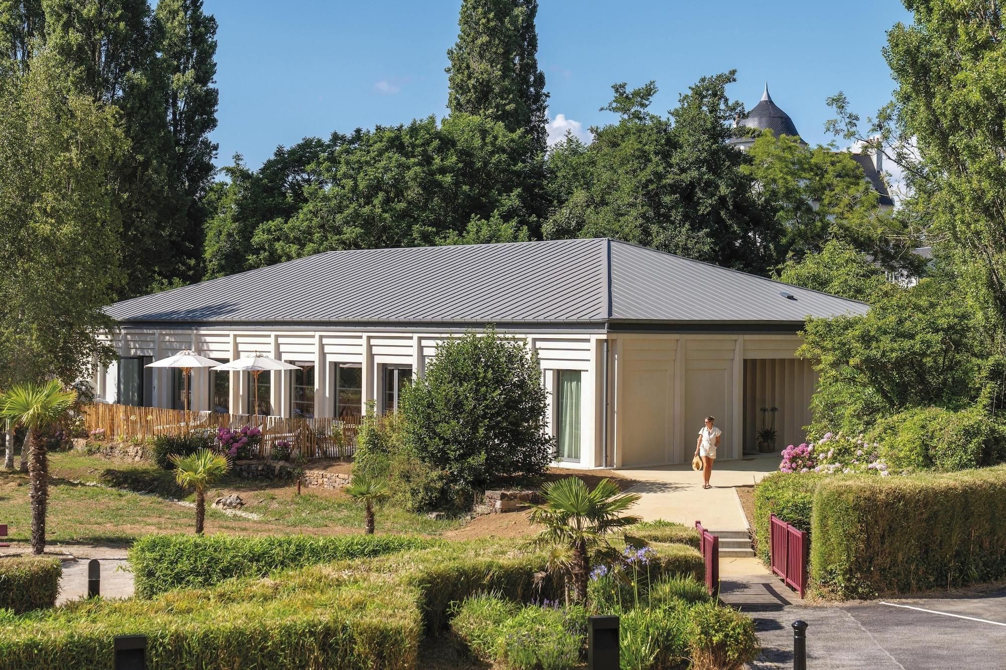 Un bâtiment moderne doté d’un patio couvert, entouré de jardins et d’arbres bien entretenus.