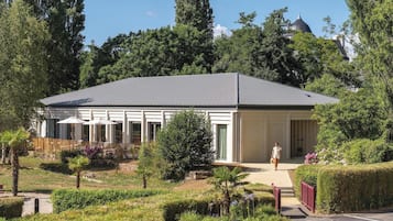 Un bâtiment moderne doté d’un patio couvert, entouré de jardins et d’arbres bien entretenus.