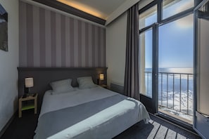 Hotellihuone, jossa on suuri sänky, kaksi yöpöytävalaisinta, merinäköala ja raidallinen seinä.