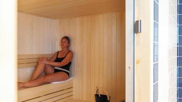 Een sauna met houten wanden en banken, een zwarte emmer en een betegelde muur met een geometrisch patroon.