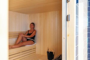 Uma sauna com paredes e bancos de madeira, um balde preto e uma parede revestida com padrão geométrico.