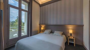 Une chambre d’hôtel avec un grand lit, deux tables de chevet avec des lampes, une vue sur la verdure et un mur à rayures.