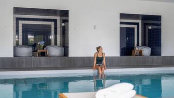 Una persona sentada junto a una piscina, con una toalla sobre una mesa, una silla y una mesita con un florero.