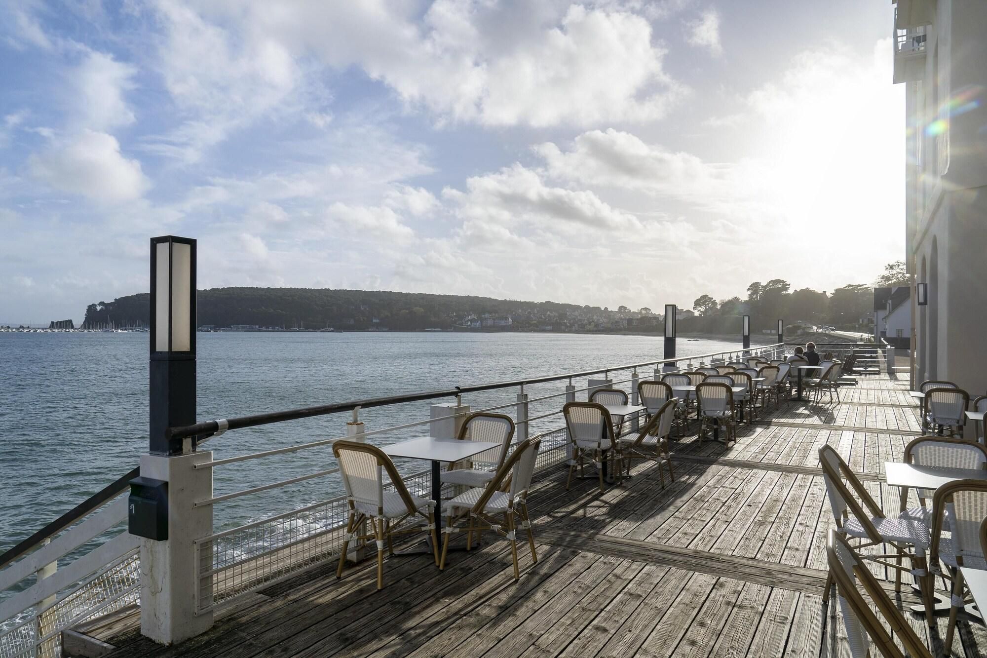 A deck with outdoor seating overlooking a body of water, a railing, and a distant shoreline.