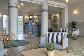 A lobby with a reception desk, seating area, and large columns. - Morgat "Le Grand Hôtel de la Mer" (Crozon)