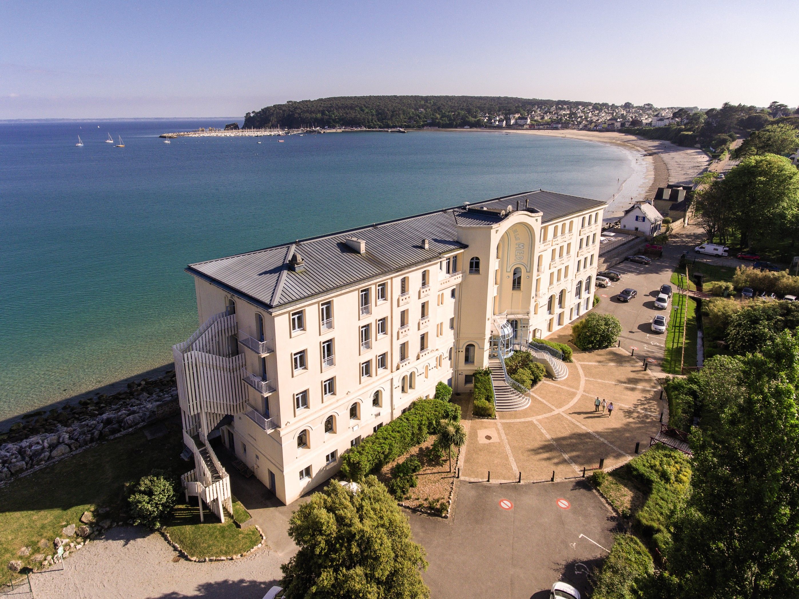 A multi-story hotel with a central courtyard, surrounded by a beach and ocean view.