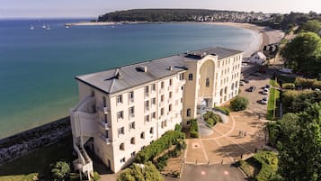 A multi-story hotel with a central courtyard, surrounded by a beach and ocean view.